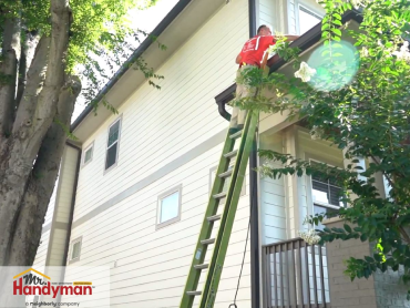 Mr. Handyman technician cleaning house gutters on a ladder during a professional home maintenance service.
