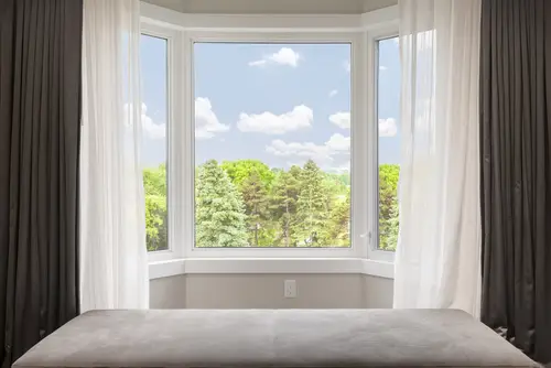 Residential bay window with drapes looking out onto a sunny forest scene