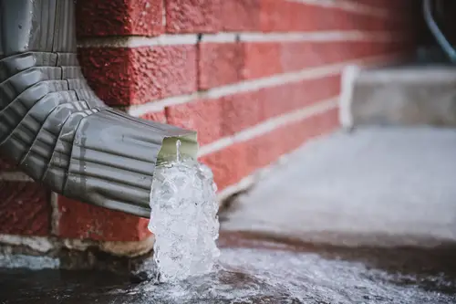 Close up of water coming out of downspout next to brick wall