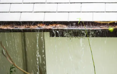 Water overflowing from clogged rain gutters on a house