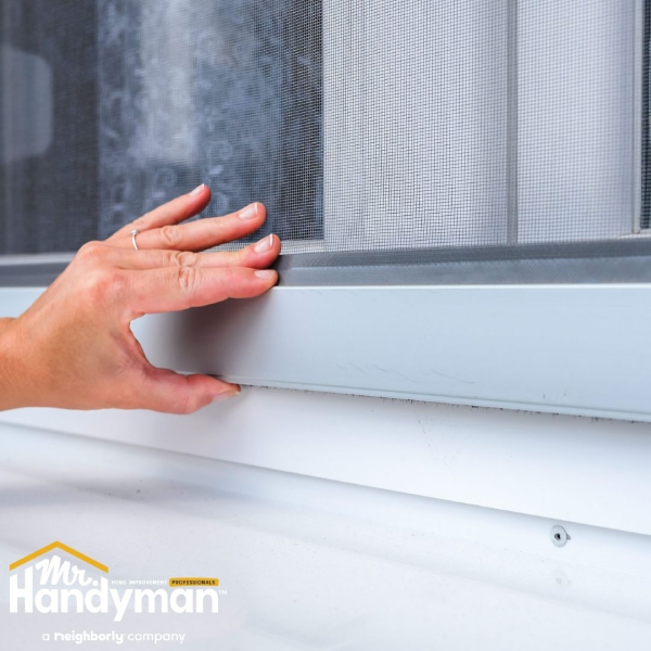 Person checking or adjusting a window screen frame along the bottom edge.