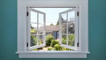 Window with trim in a blue wall, opening onto a backyard.