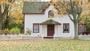 A white house surrounded by trees with a white picket fence.