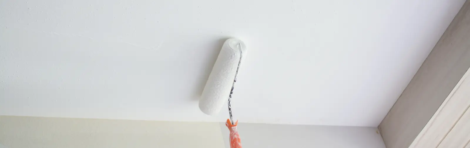 Paint roller with white paint held up against a recently repaired white ceiling, demonstrating the final stage in addressing ceiling damage or leaks.