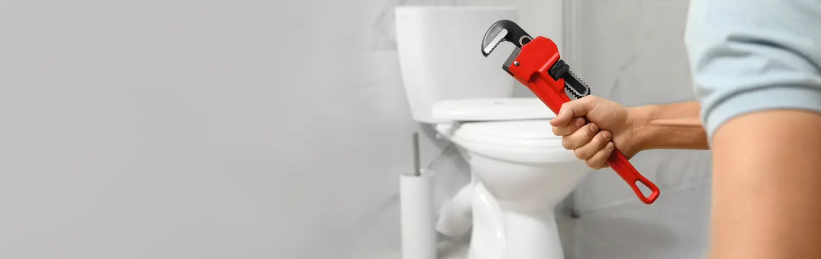 Person holding wrench near toilet leaking from the base.