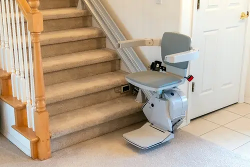 Motorized chair lift at the bottom of a carpeted residential starcase.