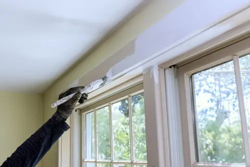 Gloved hand painting interior window trim white.