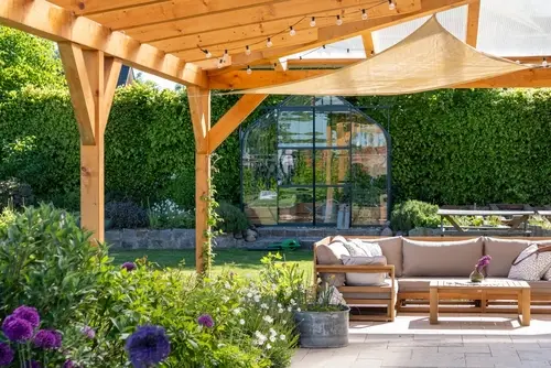 Covered patio with furniture in a blooming garden.