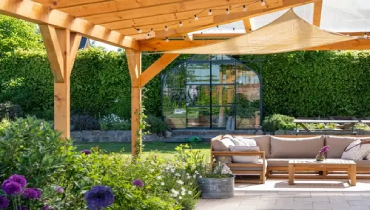 Covered patio with furniture in a blooming garden.