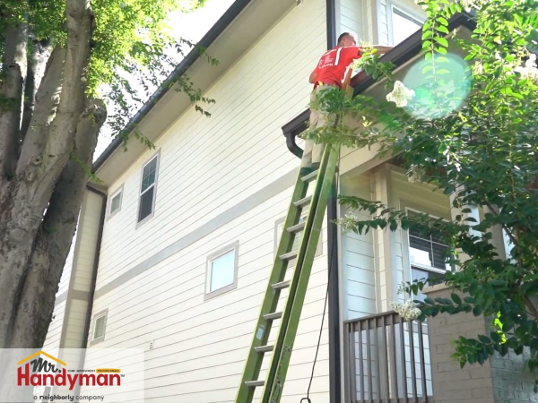 Mr. Handyman technician cleaning house gutters on a ladder during a professional home maintenance service.