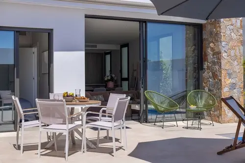 An open sliding glass door leading to a patio with green and white outdoor furniture.