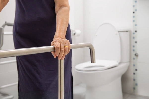 A person holding onto a metal safety grab rail in a bathroom.