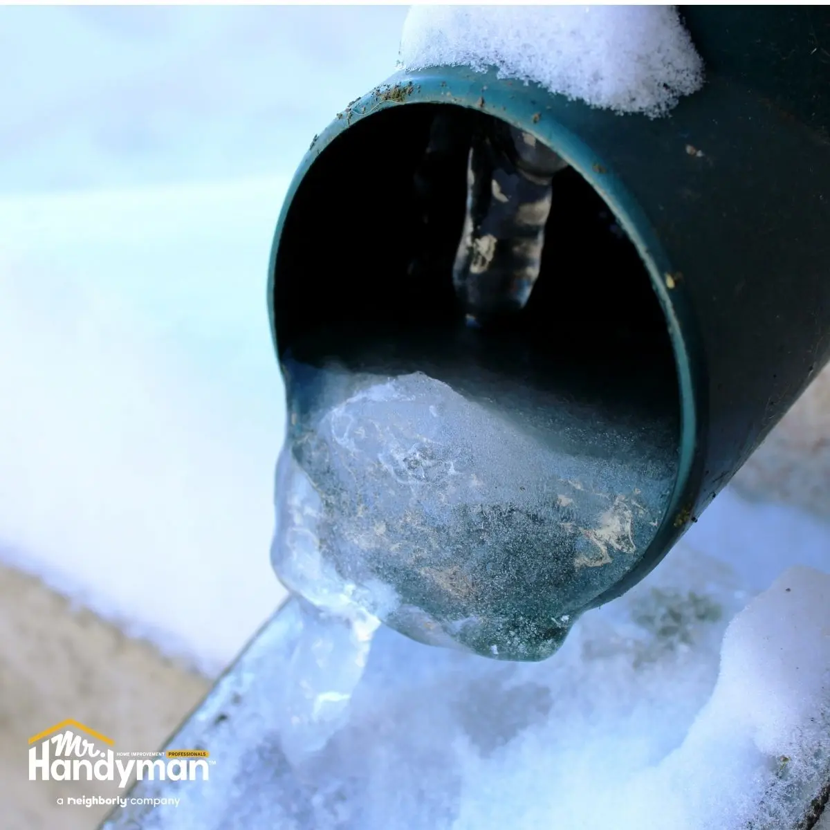 Water drips from a frozen green downspout.