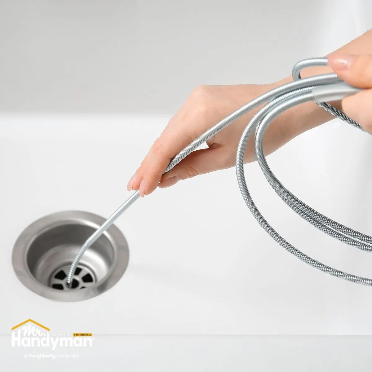 a hand uses a metal drain snake to unclog a stainless steel sink