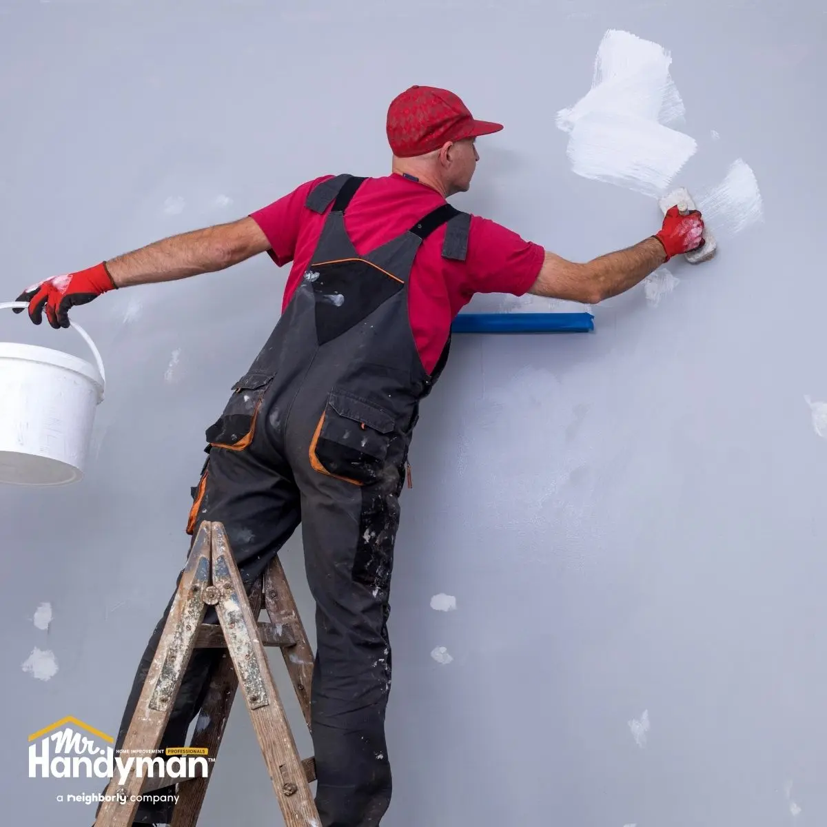 a man uses a paint apply white paint to a gray wall.