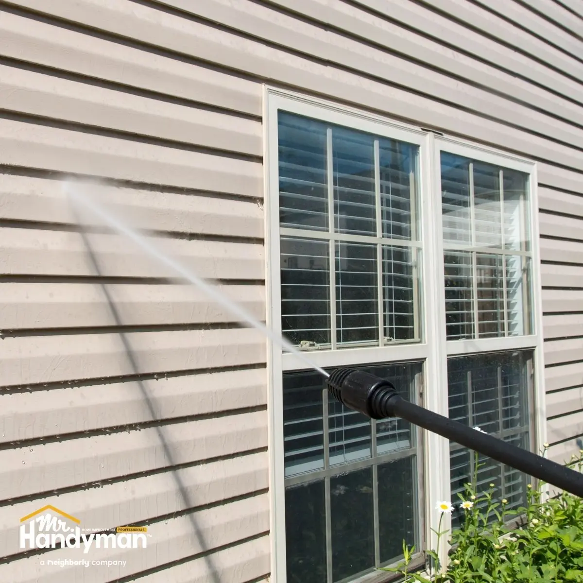 A power washer sprays water on a beige siding of a house.