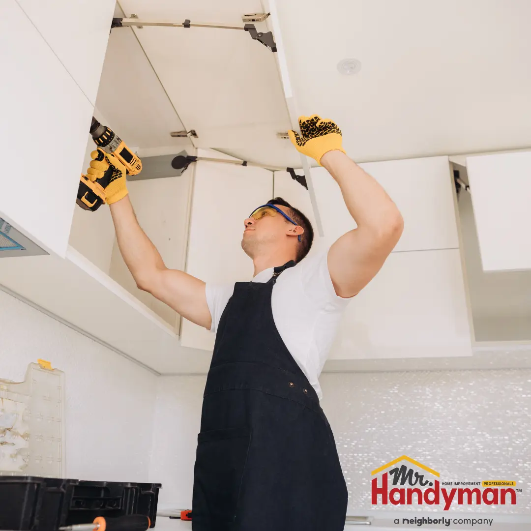 A handyman uses a power drill to install or repair a kitchen cabinet door.