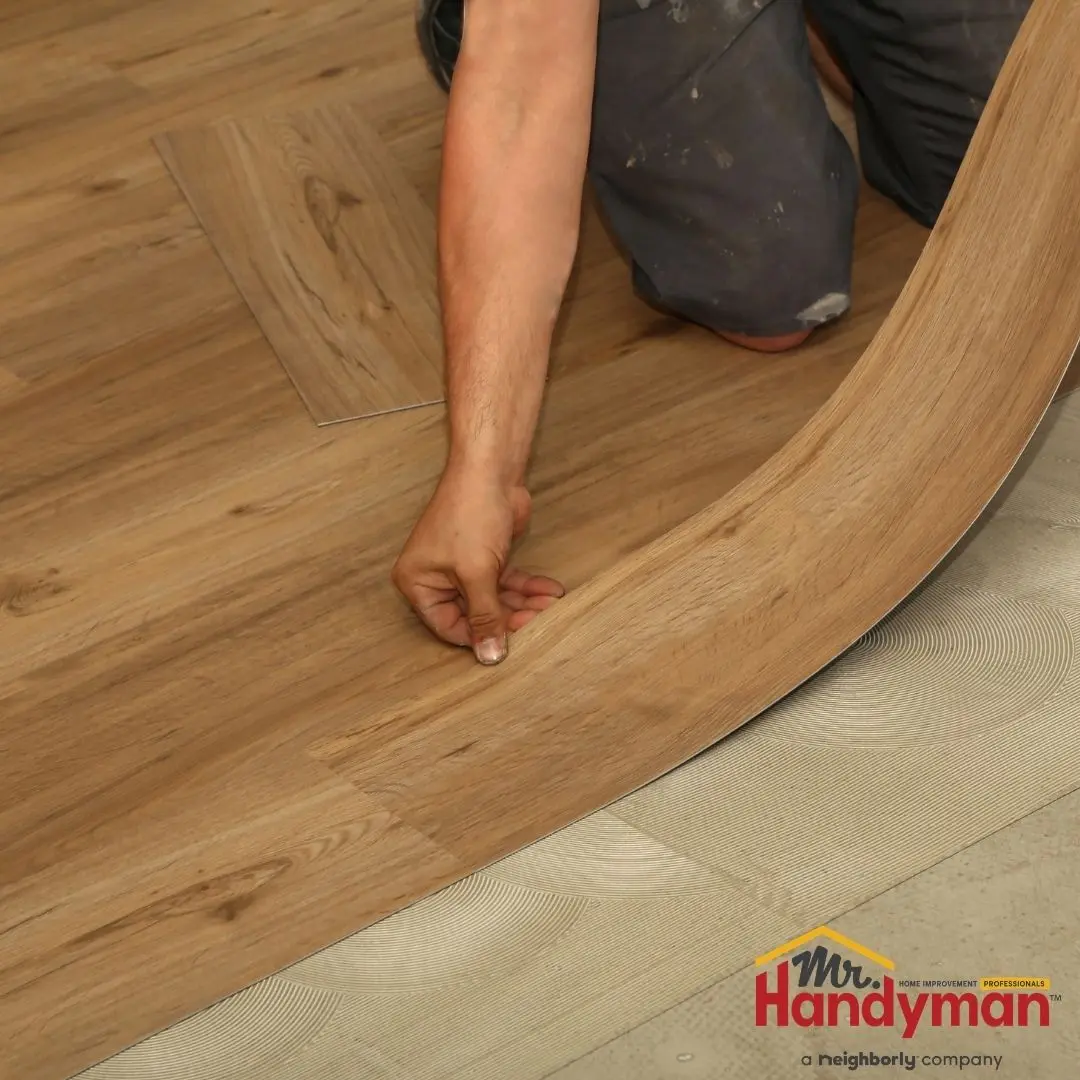 A person installing flexible wood-look vinyl flooring.