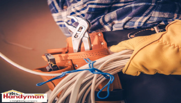 A worker holding coiled cable with tools in a tool belt.