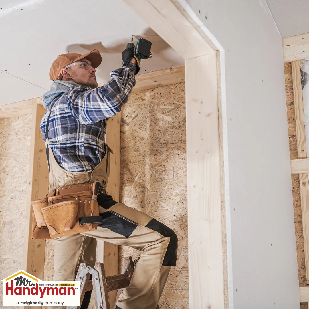 A handyman uses a drill on a partially constructed wall in a house.