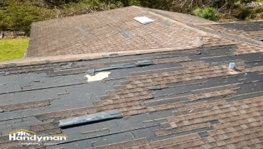 Damaged roof with missing shingles exposes black underlayment.