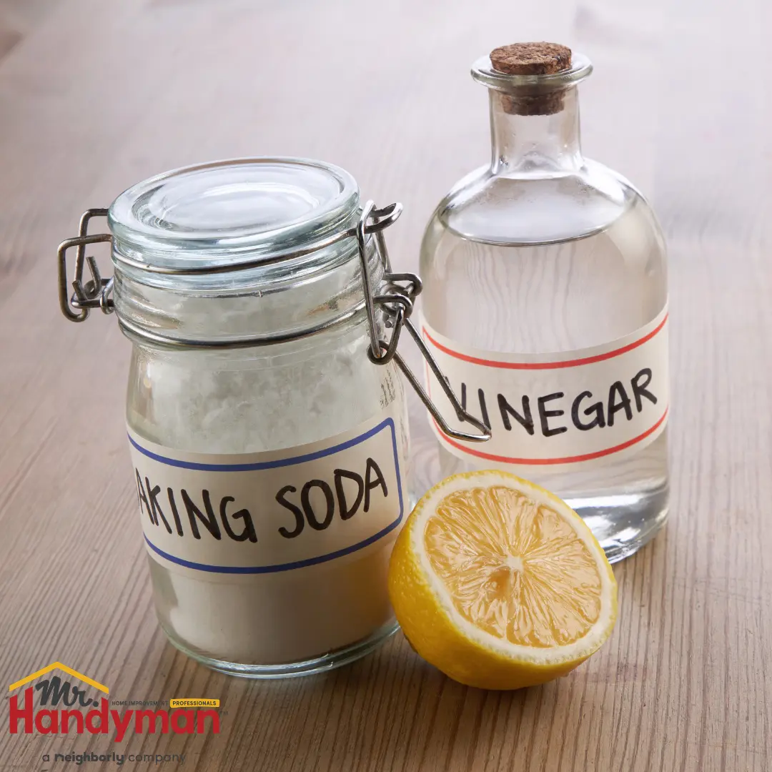 glass jars labeled baking soda and vinegar with a halved lemon on a wooden surface