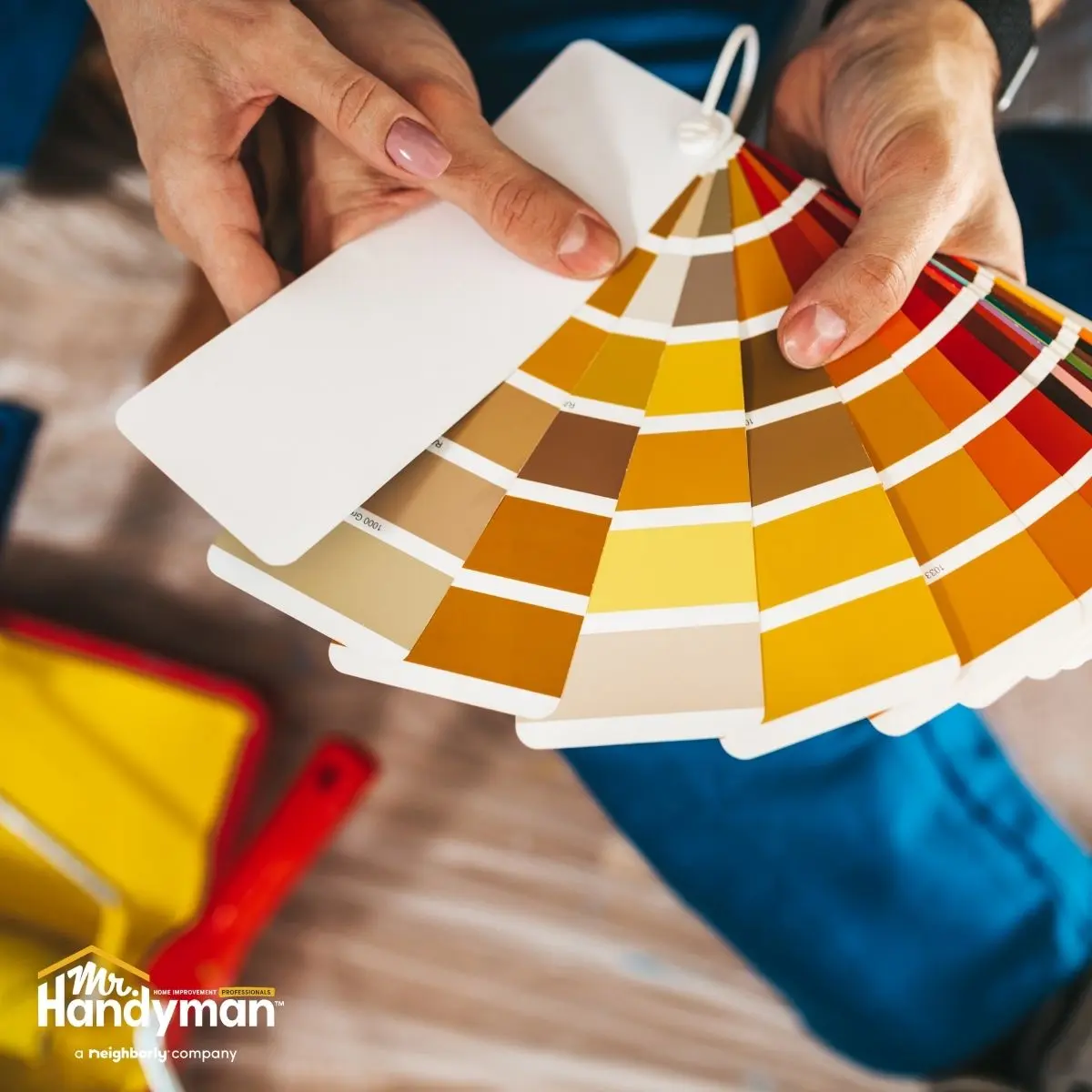 -hands holding a fan of paint swatches in warm tones of yellow and orange.