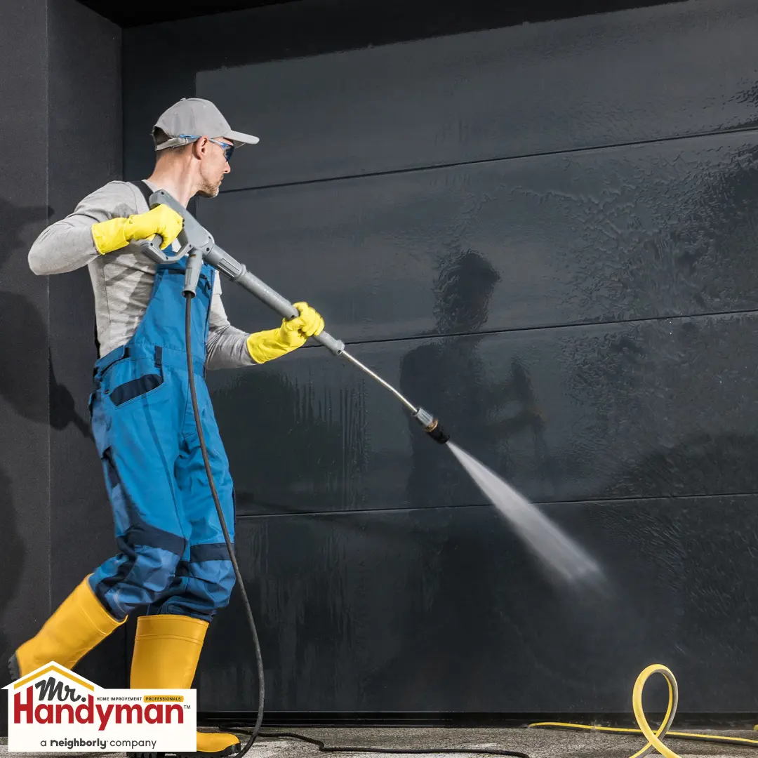 A person uses a power washer on a dark, wet wall.