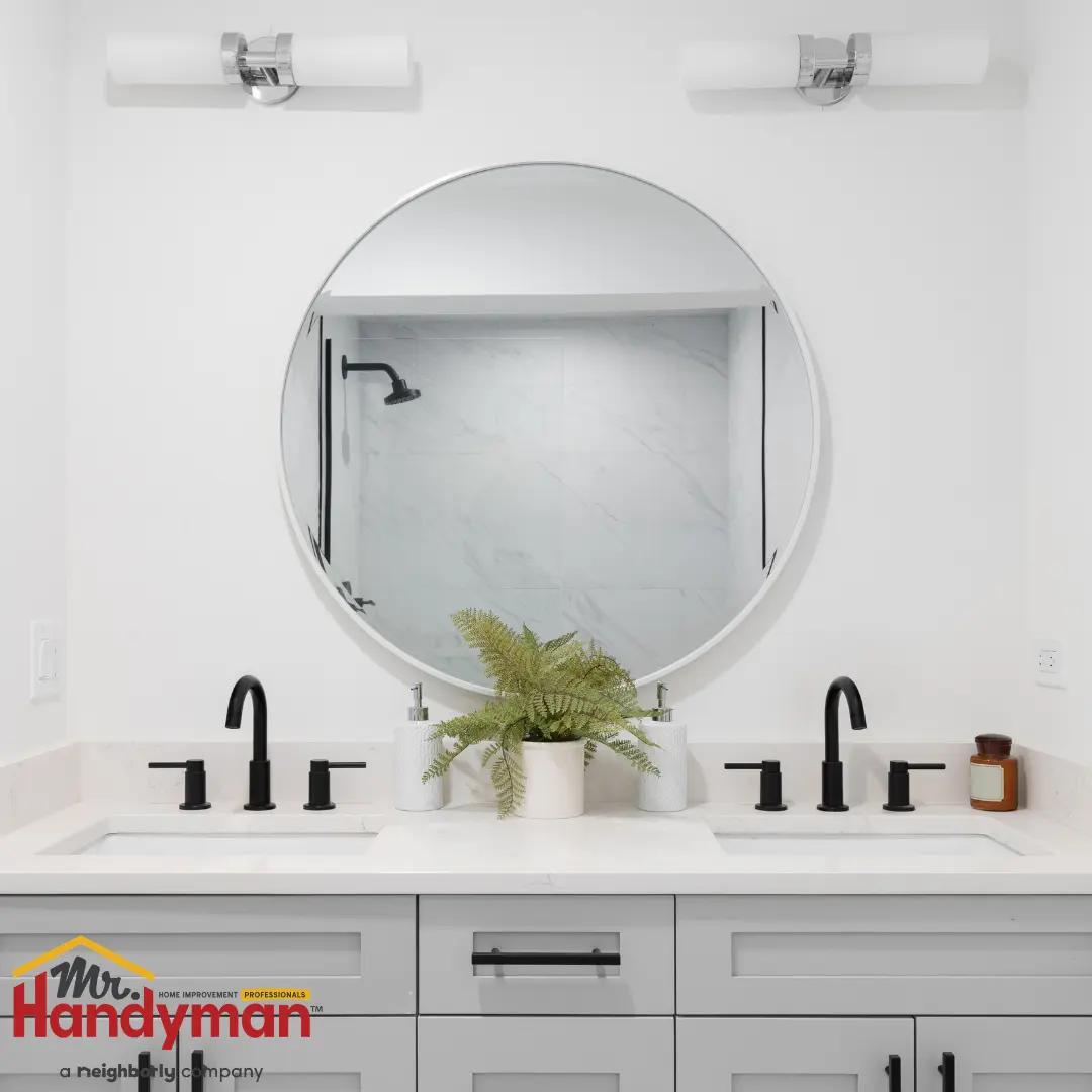 A modern double-sink bathroom vanity with white cabinets, black faucets, and a large round mirror.