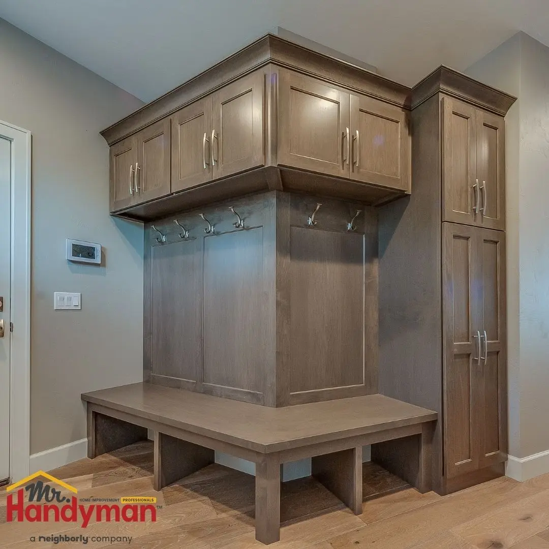 Brown wooden mudroom bench with overhead cabinets, vertical storage, and metal coat hooks.