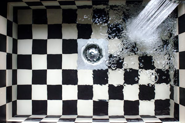 Photo of the inside of a kitchen sink. The sink is black-and-white checkered, and water is running into it, filling the sink.