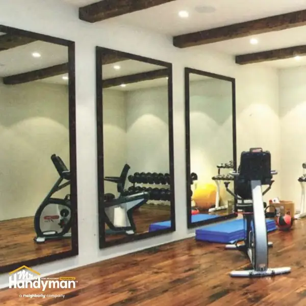 Mr. Handyman technician professionally installing large gym mirrors
