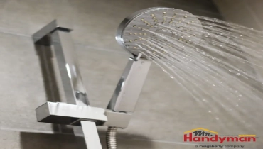 Modern chrome showerhead mounted on a tiled bathroom wall, spraying multiple streams of water.