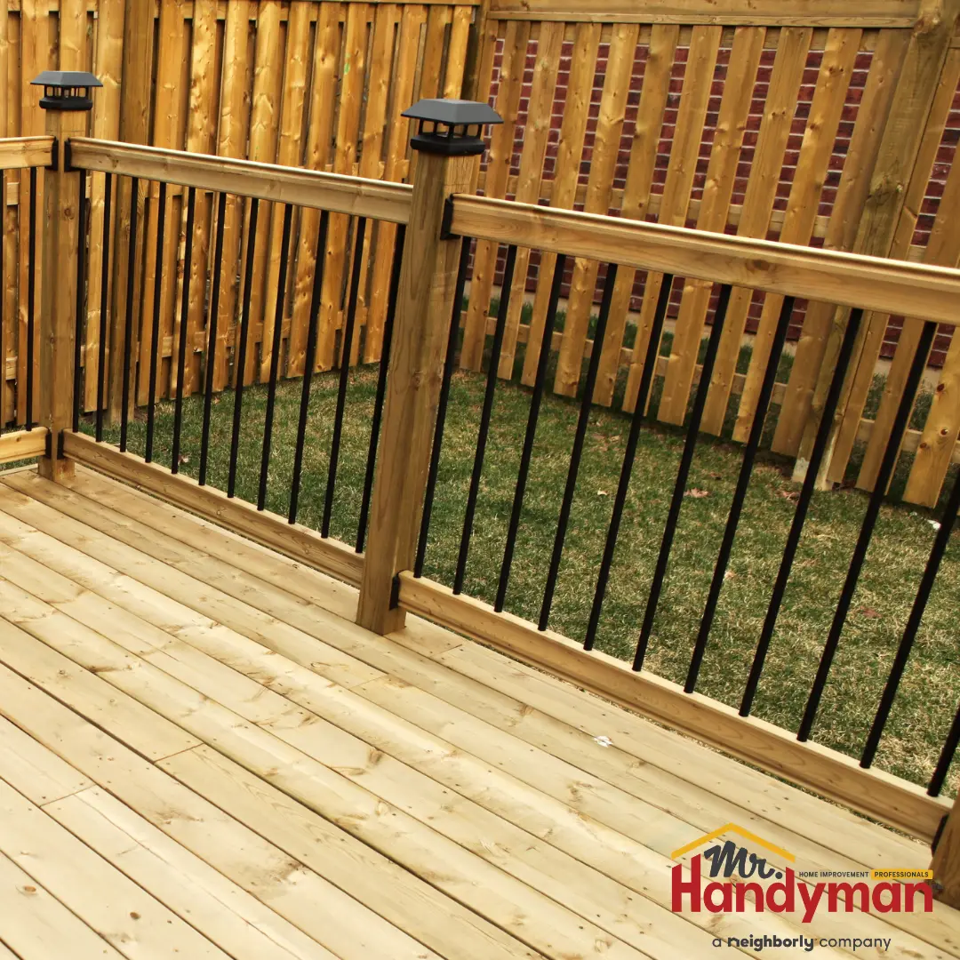 A newly constructed wooden deck with black metal balusters and matching posts, bordered by a tall wooden fence.
