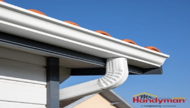 close-up of a white gutter system with a downspout leading away from the roofline of a house.