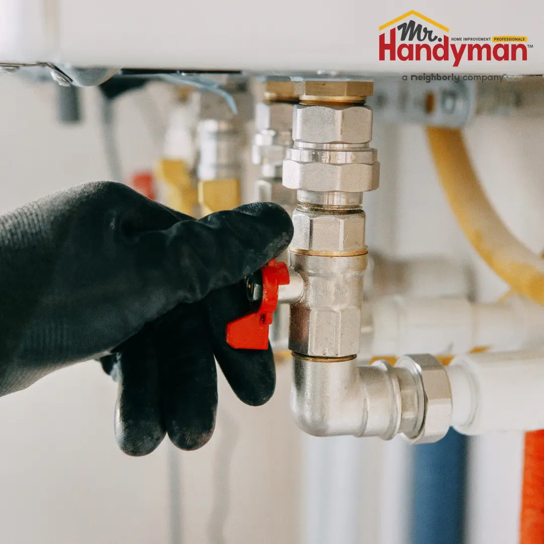 A Mr. Handyman technician adjusting a red valve on a metal pipe fitting connected to a household heating system.