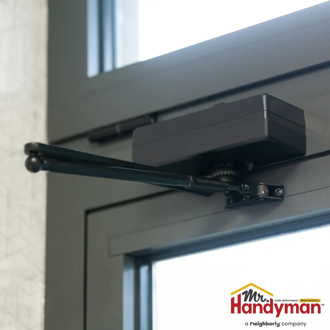 A black automatic door closer is mounted to the top frame of a dark glass door.