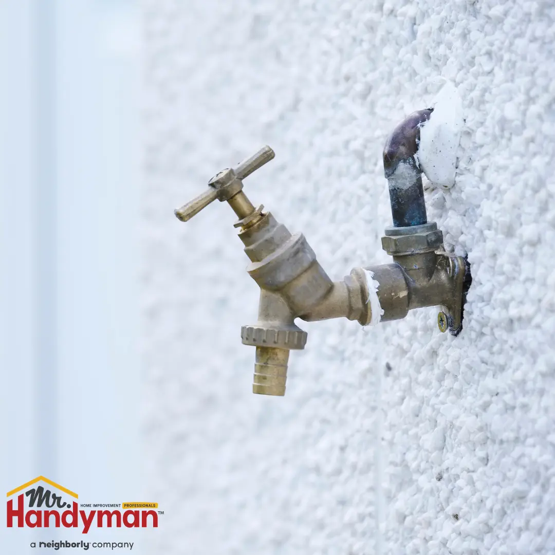 outdoor brass water faucet attached to a textured white wall with a small pipe connection