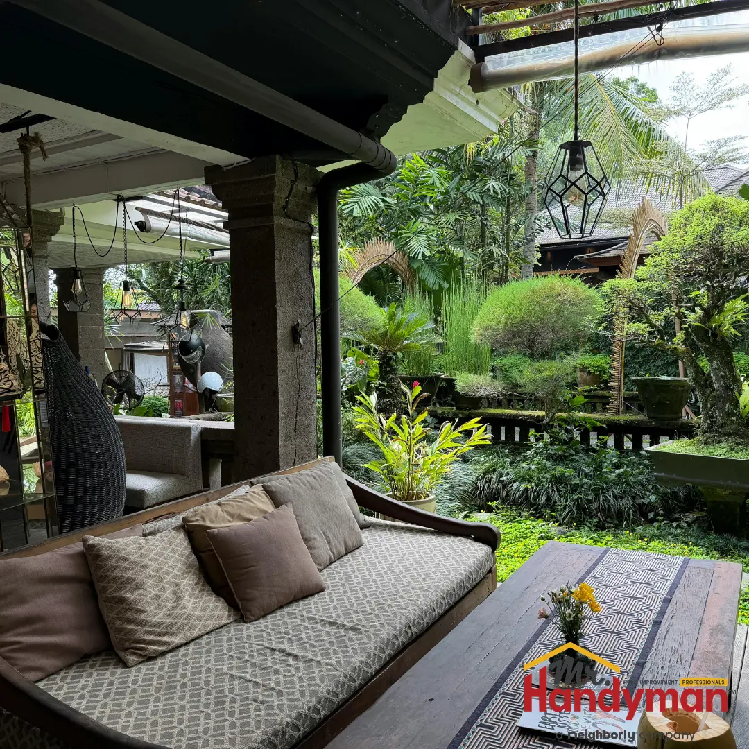A cozy Balinese-style porch with a cushioned sofa, hanging lanterns, and a view into a lush tropical garden.