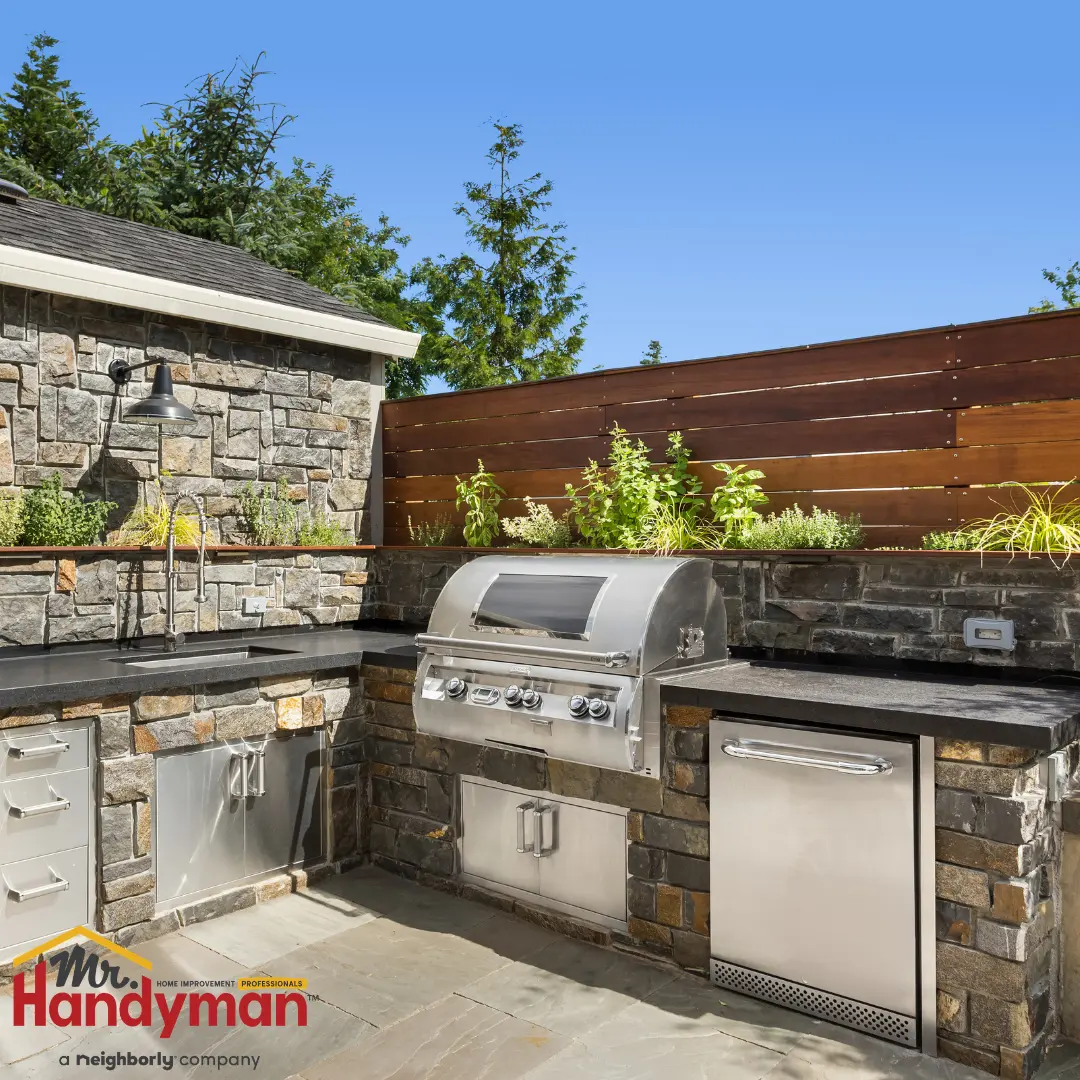 An outdoor stone kitchen with a built-in stainless steel grill, sink, and mini-fridge.
