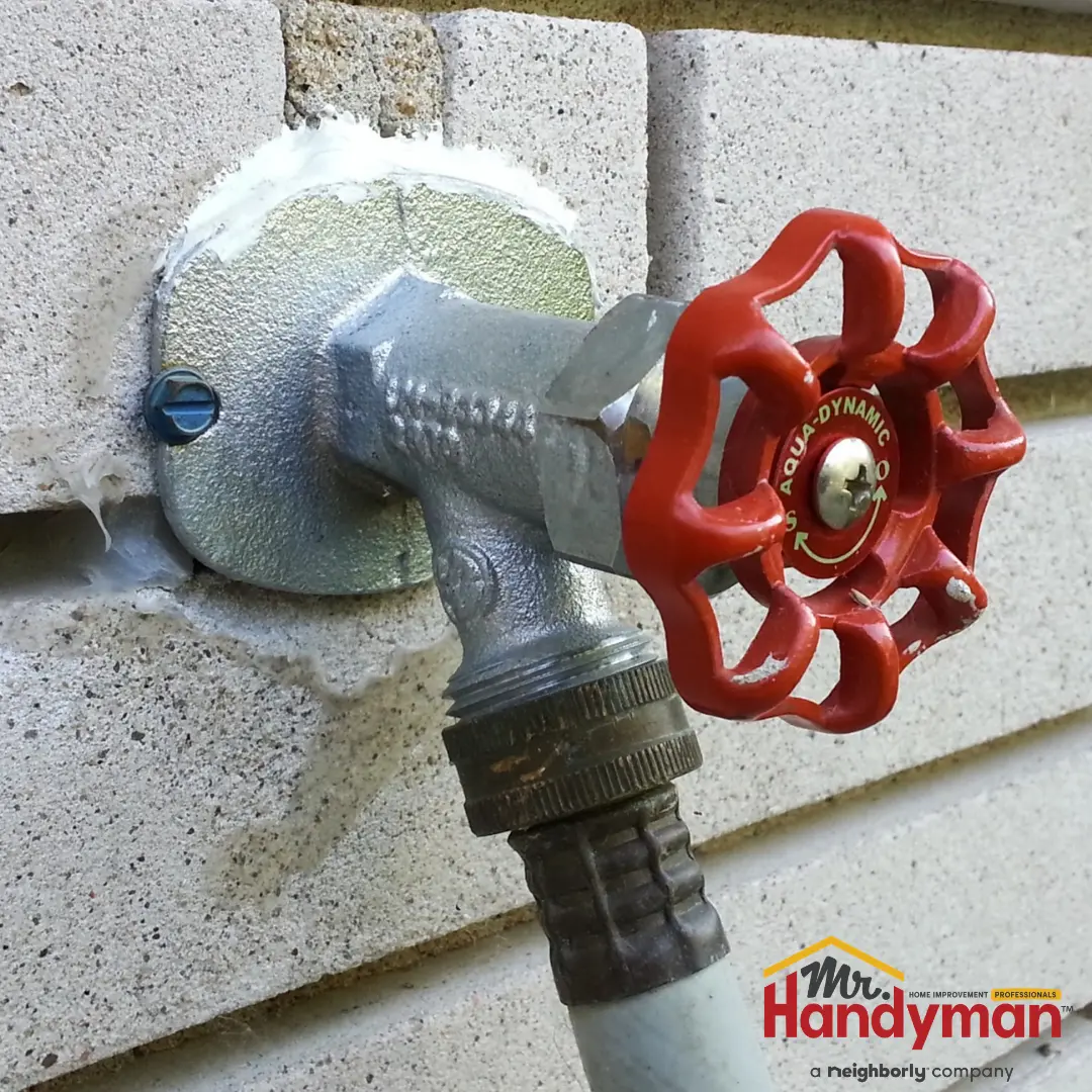 An outdoor frost-free water spigot with a red wheel handle.