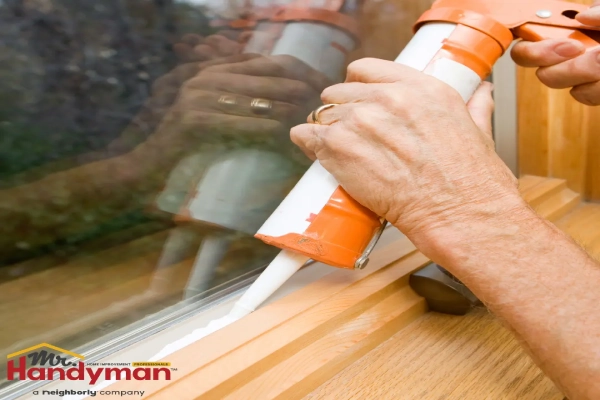 Mr. Handyman technician applying sealant to the edge of a wooden window frame using a caulking gun.