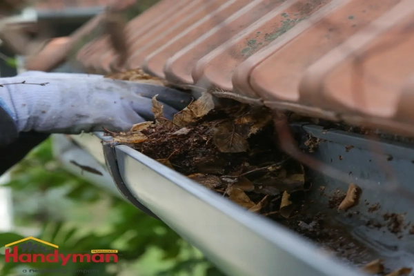 Mr. Handyman technician clearing debris from a gutter beneath a tiled roof.