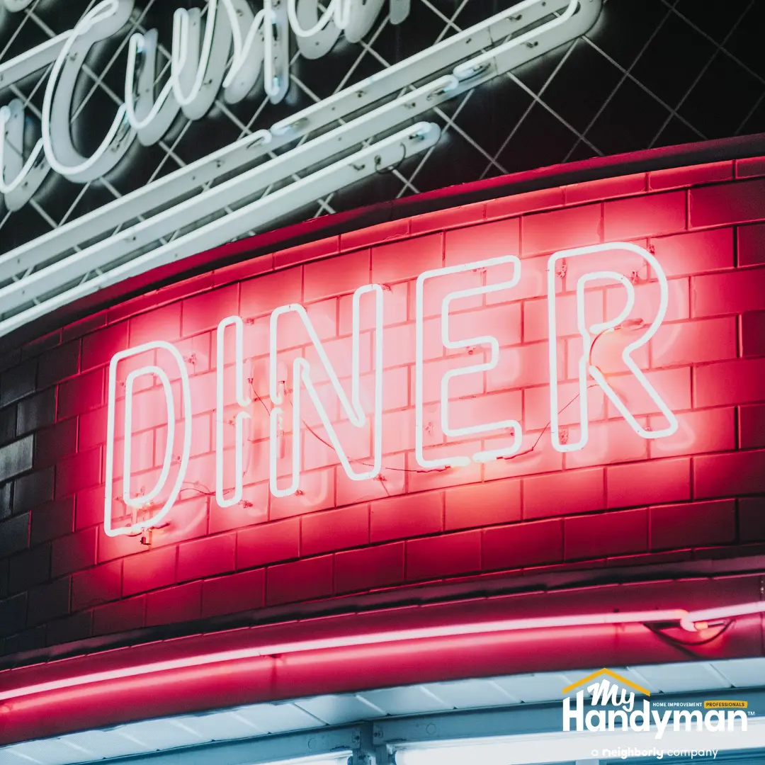 Neon pink "DINER" sign glowing on a red tiled exterior wall.