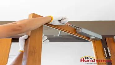 person wearing gloves installs a metal door closer on a wooden door frame indoors