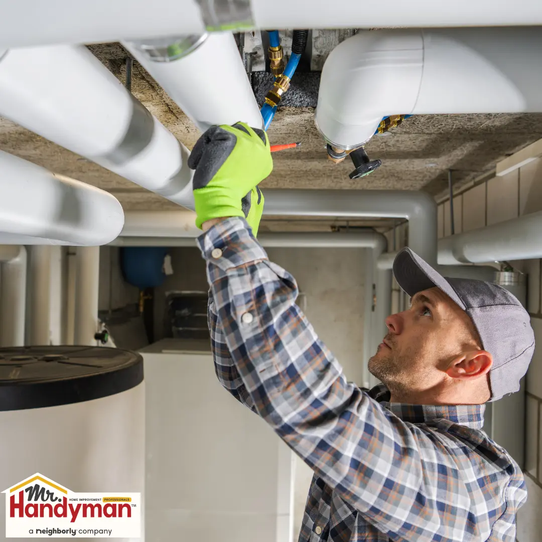 A plumber repairing pipes on a basement ceiling.