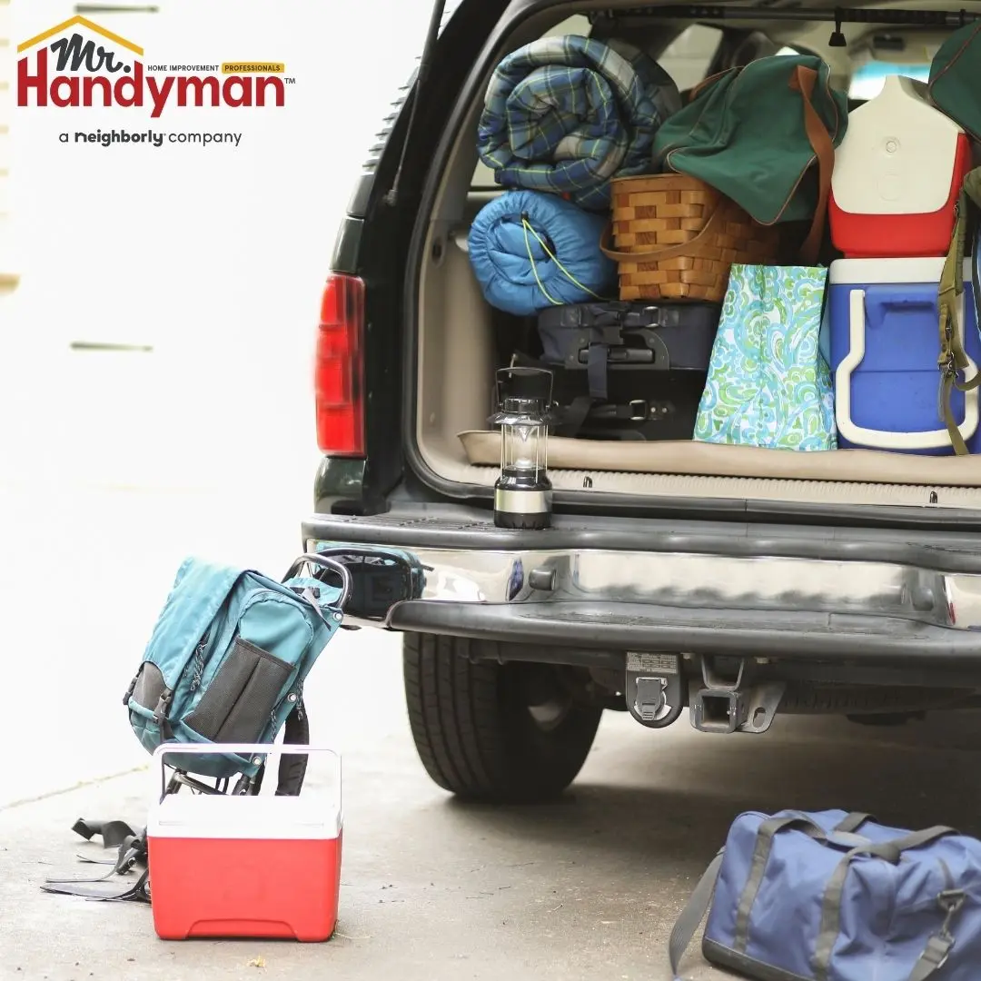 The open trunk of a vehicle packed with camping gear, including coolers, sleeping bags, and a lantern.