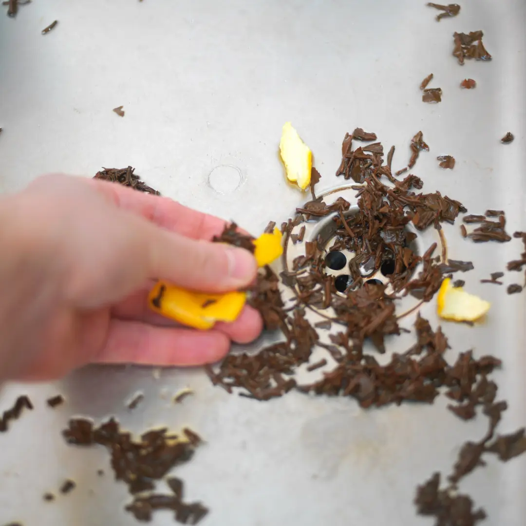 A person using a yellow sponge to scrub away brown, fibrous material from a kitchen sink drain.