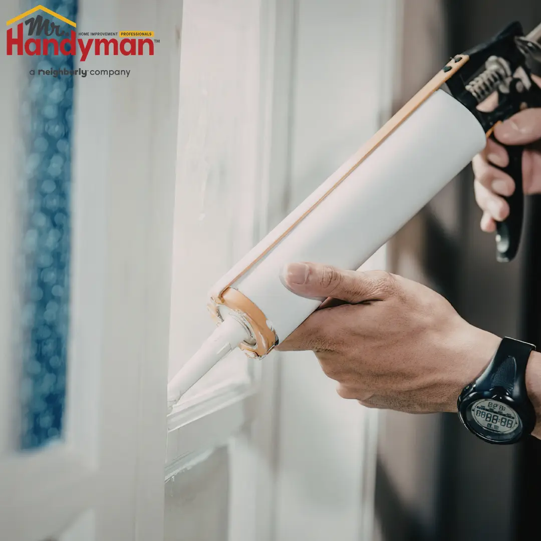 A person uses a caulking gun to apply white caulk along the frame of a window.