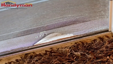 A damaged window screen has a noticeable rip and is tearing.